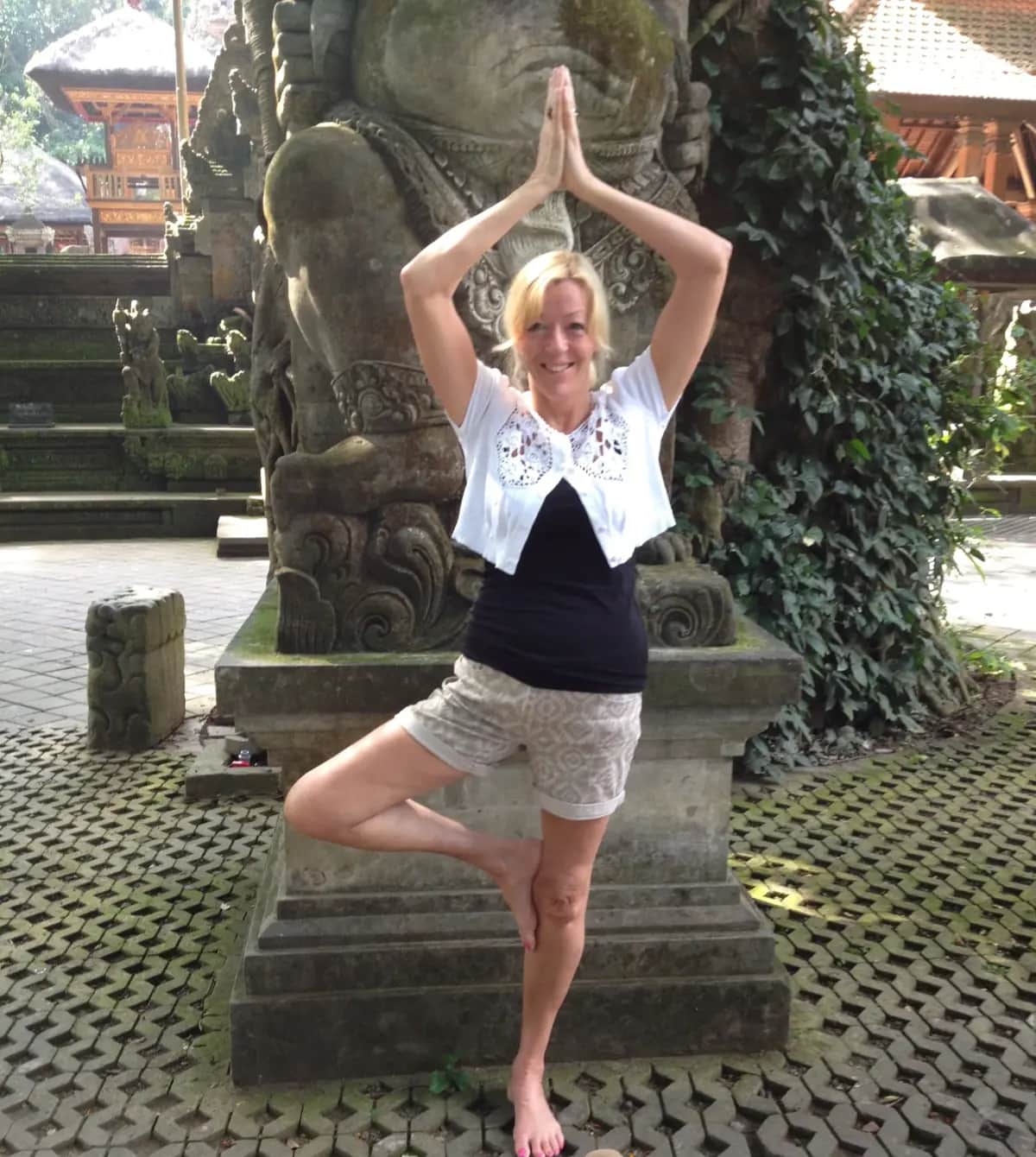 Vivien in tree pose by a stone statue during her spiritual journey