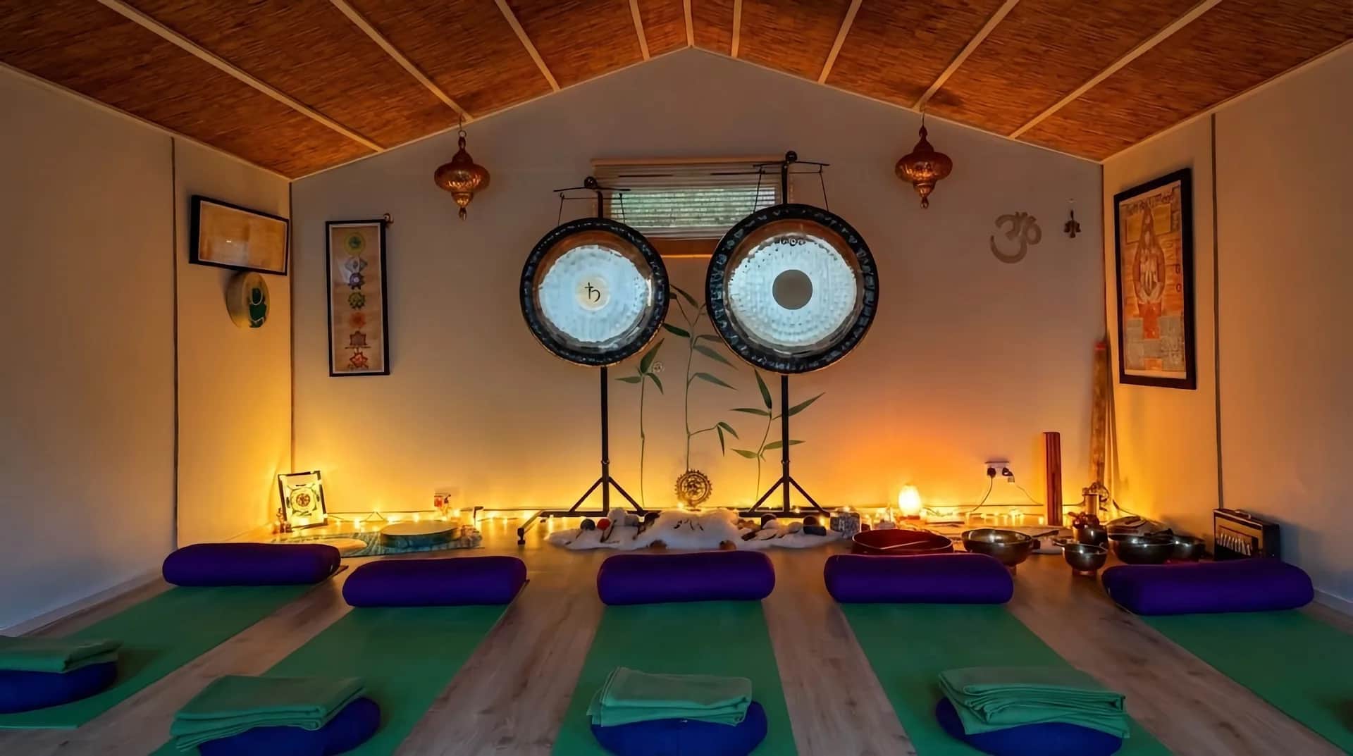 Gong bath setup at The Yoga Den with two large gongs, purple bolsters, and warm ambient lighting