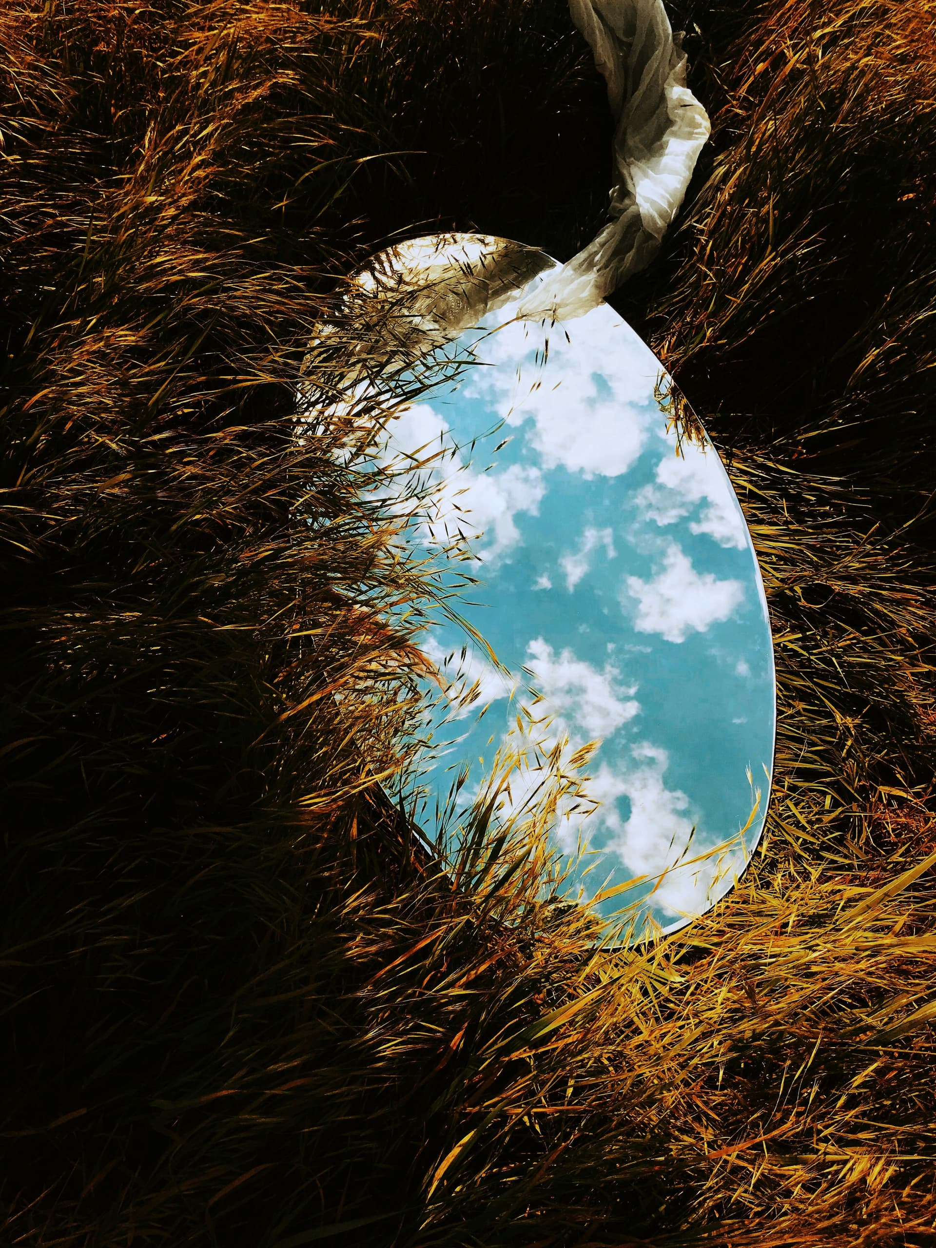 A round mirror lying in golden grass, reflecting the sky and clouds